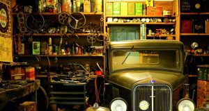 A garage interior basked in warm light and filled with a lot of trinkets and an old car on one side.