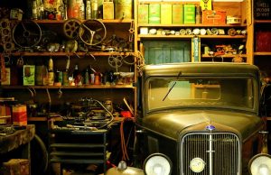 A garage interior basked in warm light and filled with a lot of trinkets and an old car on one side.