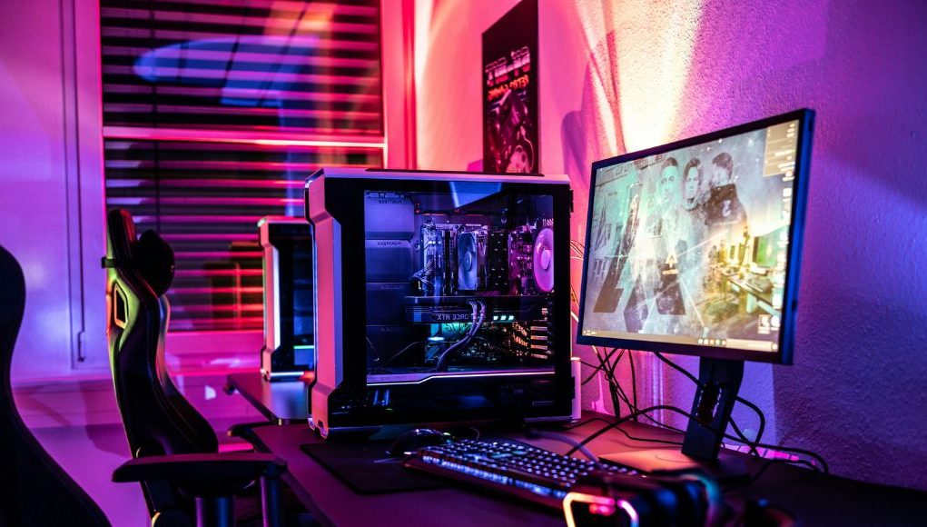 A gaming PC setup with bright red, orange, purple, and blue lights at the back of the monitor.