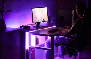Budget vs Premium Gaming Lighting – What’s Worth It? A man sitting in front of a PC in a dark room with an under desk purple light.