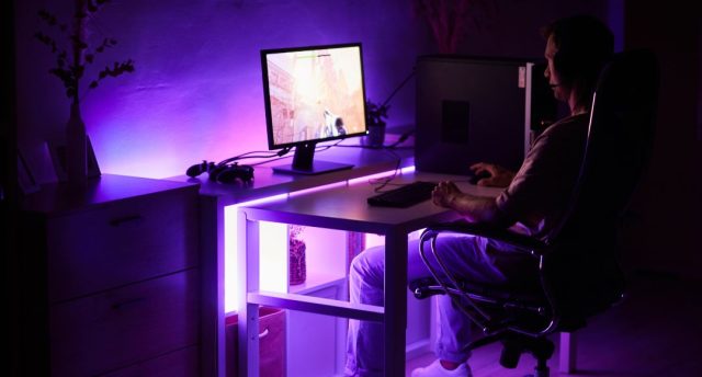 Budget vs Premium Gaming Lighting – What’s Worth It? A man sitting in front of a PC in a dark room with an under desk purple light.