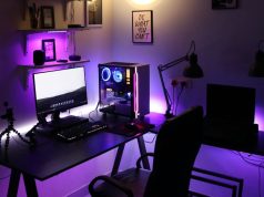 A PC setup in a dim room with a warm overhead light and a purple under desk lighting.