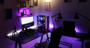 A PC setup in a dim room with a warm overhead light and a purple under desk lighting.