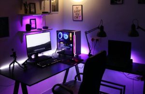 A PC setup in a dim room with a warm overhead light and a purple under desk lighting.