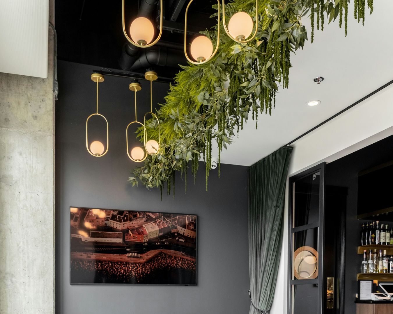 The facade of a commercial space which features warm statement lighting with hanging plants.