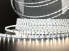 A roll of Simple Lighting LED strip light that's glowing with a bit of a warm white light, on a dark surface and background.