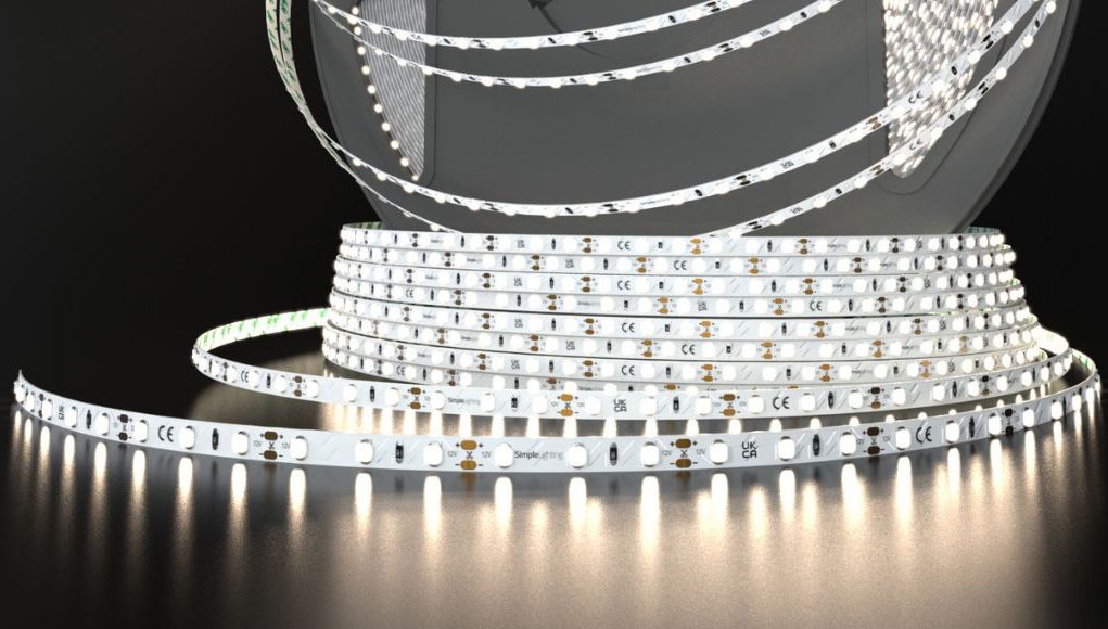 A roll of Simple Lighting LED strip light that's glowing with a bit of a warm white light, on a dark surface and background.