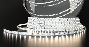 A roll of Simple Lighting LED strip light that's glowing with a bit of a warm white light, on a dark surface and background.