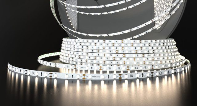 A roll of Simple Lighting LED strip light that's glowing with a bit of a warm white light, on a dark surface and background.