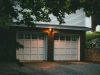 An exterior view of a home garage with a white door and two warm lights at the centre.