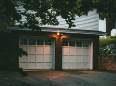 Garage Lighting Ideas for a Brighter, Safer Space An exterior view of a home garage with a white door and two warm lights at the centre.