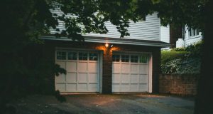 An exterior view of a home garage with a white door and two warm lights at the centre.