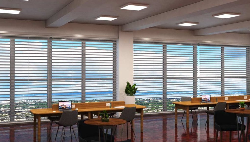 An open office space with two long wooden desks near two large windows.