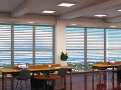 An open office space with two long wooden desks near two large windows.
