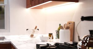 A bright kitchen countertop with various kitchen stuff with under-cabinet strip lighting for illumination.
