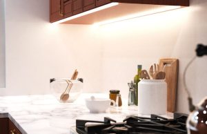A bright kitchen countertop with various kitchen stuff with under-cabinet strip lighting for illumination.
