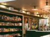 An view of a commercial space from the outside with shelves, the counter, and warm lights visible.