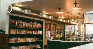 An view of a commercial space from the outside with shelves, the counter, and warm lights visible.