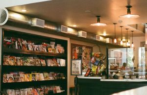 Retail Lighting That Sells: Techniques for Shops & Showrooms An view of a commercial space from the outside with shelves, the counter, and warm lights visible.