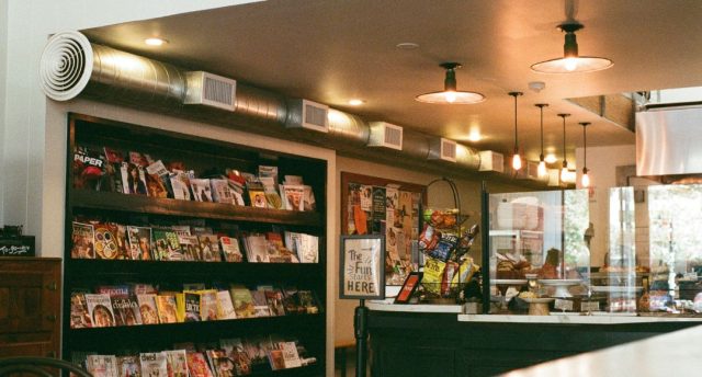 Retail Lighting That Sells: Techniques for Shops & Showrooms An view of a commercial space from the outside with shelves, the counter, and warm lights visible.