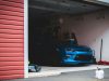 Best Smart Lighting Options for Your Garage A blue car is parked inside an open dark garage.