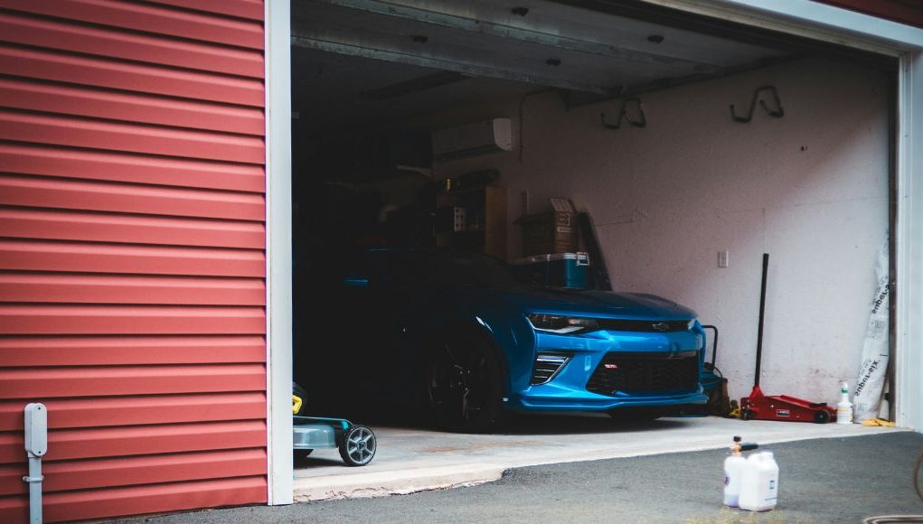 A blue car is parked inside an open dark garage.