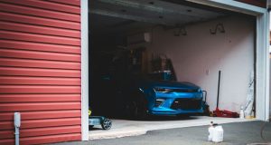 A blue car is parked inside an open dark garage.
