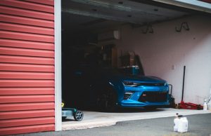 Best Smart Lighting Options for Your Garage A blue car is parked inside an open dark garage.