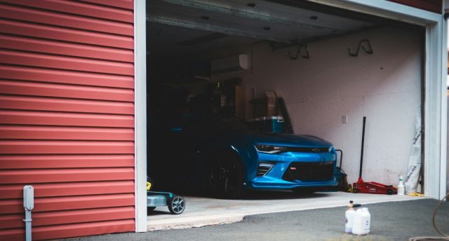 Best Smart Lighting Options for Your Garage A blue car is parked inside an open dark garage.