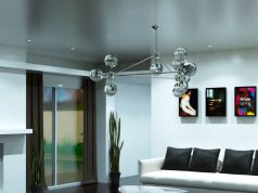 A living room with white sofa and black pillows and a silver hanging statement light.