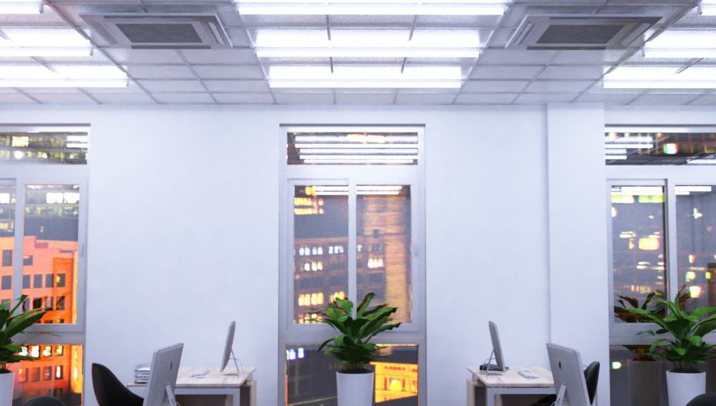An office with windows overlooking a city, its ceiling is installed with multiple tube lights.