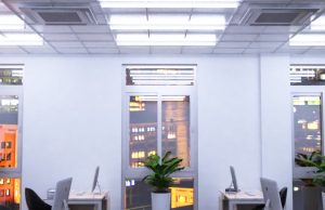 An office with windows overlooking a city, its ceiling is installed with multiple tube lights.