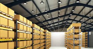 An image of a warehouse with shelves filled with boxes and the ceiling filled with high bay lights.