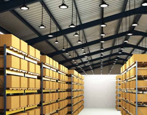 An image of a warehouse with shelves filled with boxes and the ceiling filled with high bay lights.