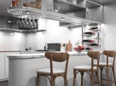 A kitchen with a bar counter and three chairs beside it, multiple under cabinet lights are illuminating the space.