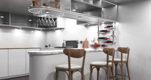 A kitchen with a bar counter and three chairs beside it, multiple under cabinet lights are illuminating the space.