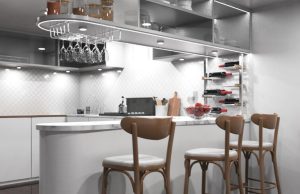 A kitchen with a bar counter and three chairs beside it, multiple under cabinet lights are illuminating the space.