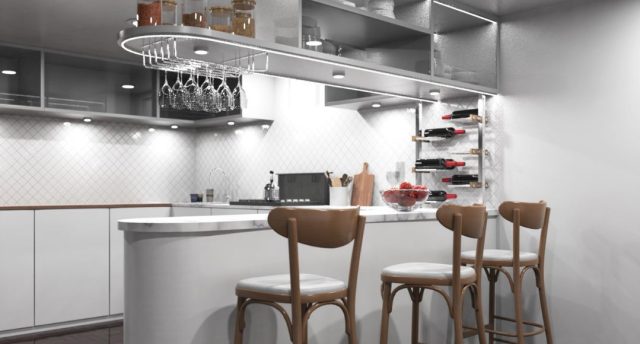 Create the Perfect Mood for Any Moment with Smart Lighting Automation A kitchen with a bar counter and three chairs beside it, multiple under cabinet lights are illuminating the space.