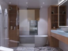 Avoid These Common Bathroom Lighting Mistakes A modern bathroom with wooden cabinets and sink area, the bath tub and shower area are behind a glass wall.