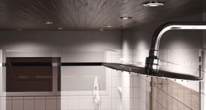 A closeup of a showerhead in the foreground, multiple downlights on the wooden ceiling, and the upper part of the bathroom walls.