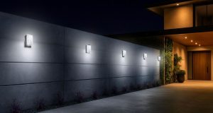 An outdoor wall of a modern home with five LED bulkhead lights installed and glowing with bright white light.