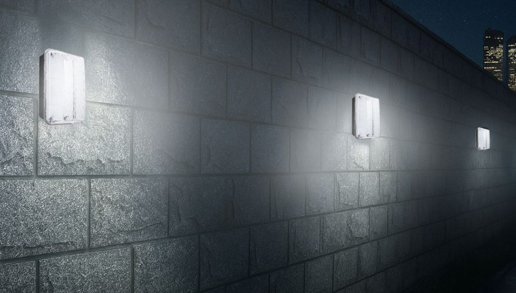 An exterior wall installed with multiple IP65 LED bulkhead lights, a skyscraper is seen in the background.