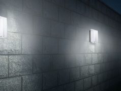 An exterior wall installed with multiple IP65 LED bulkhead lights, a skyscraper is seen in the background.