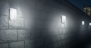 An exterior wall installed with multiple IP65 LED bulkhead lights, a skyscraper is seen in the background.