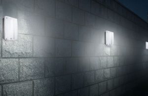 An exterior wall installed with multiple IP65 LED bulkhead lights, a skyscraper is seen in the background.