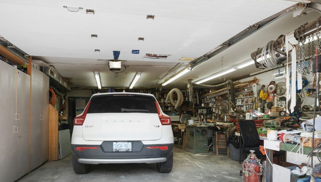 Efficient Garage 1 A white car parked in a garage with one side of the space filled with random things.