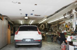 A white car parked in a garage with one side of the space filled with random things.