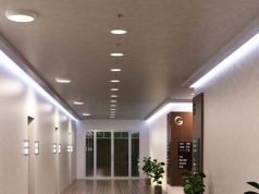 A hallway with multiple round bulkhead lights installed on the ceiling and LED strip lights glowing on both sides