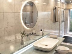 How to Safely Install Bathroom Lighting: What You Need to Know A modern bathroom with a round LED mirror over a vanity, and the shower area is behind a glass partition.