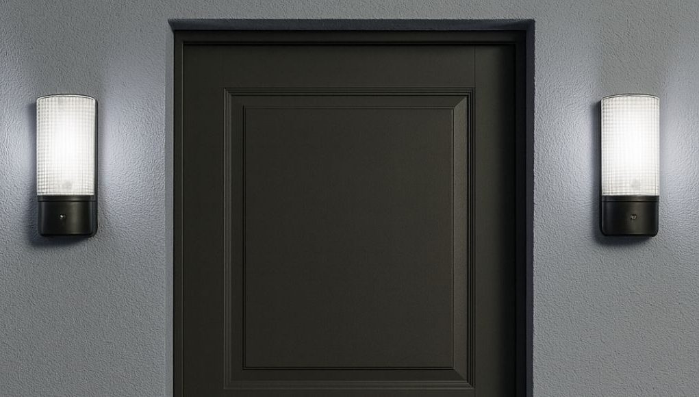A dark grey door with two bulkhead lights installed on both sides, glowing with natural white light.